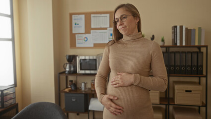 Pregnant woman stands in an office holding her belly, surrounded by office equipment and shelves, capturing a serene moment of expectation and work-life balance.