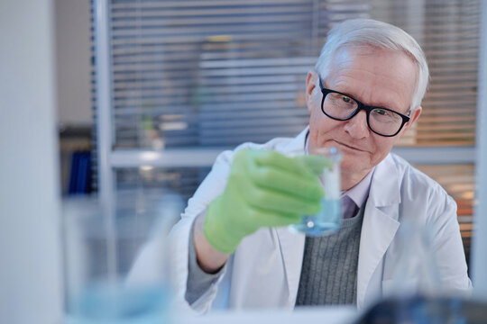 Portrait of senior Caucasian man wearing glasses and lab coat holding laboratory glassware with gloved hand, conducting scientific experiment in modern laboratory setting - Powered by Adobe