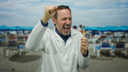 Middle-aged man in white coat celebrates holding toothbrush on sunny seaside with beach umbrellas.