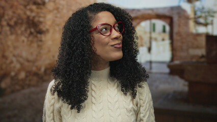 Woman wearing red glasses and cream sweater smiling with visible face in historic street; joyful connection.