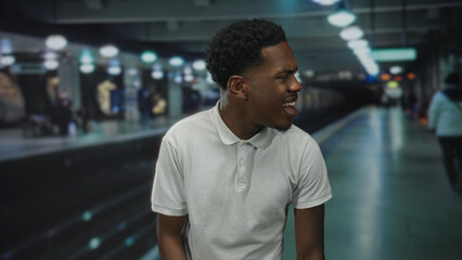Man grimaces on empty train station platform wearing white polo shirt; frustration delay commute hurry.
