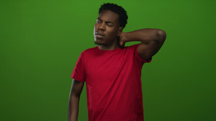 Man holds neck in studio while wincing from muscle tension and leaning sideways wearing a red shirt; discomfort.
