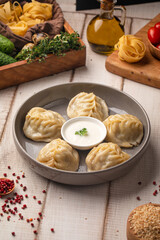 Steamed manty dumplings with meat filling served with creamy sauce on a rustic wooden table