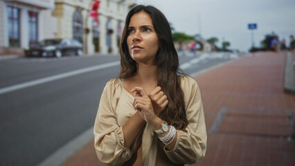 Fototapeta premium Woman on street crossing and pointing with fingers, visible hands near chest, urban sidewalk and road in frame; concern.