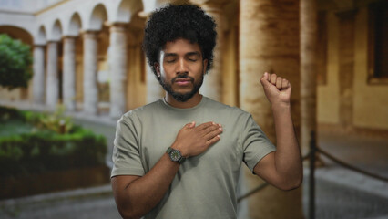 African american man outdoors with eyes closed, hand on chest, making a pledge with architectural columns in the background.