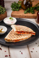 Chicken quesadilla served on a black plate with sauces and fresh herbs