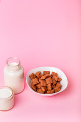Dry breakfast and milk. Dry sweet breakfast - Chocolate corn pillows and milk on pink background. Quick and nutritious breakfast. Pink background.