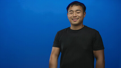 Young chinese man wearing black t shirt smiling extends hand for handshake in blue studio; welcome...