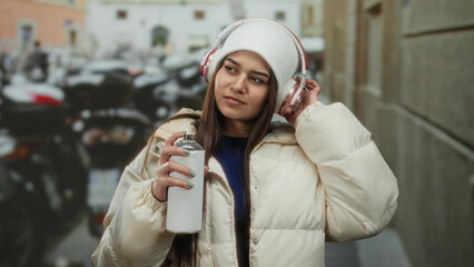 Woman in park wearing headphones and holding spray can, showcasing urban graffiti culture with emphasis on street art, creativity, and outdoor expression during winter time.