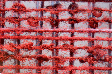 Close-up abstract texture of a red woven mesh net with frayed threads and knots
