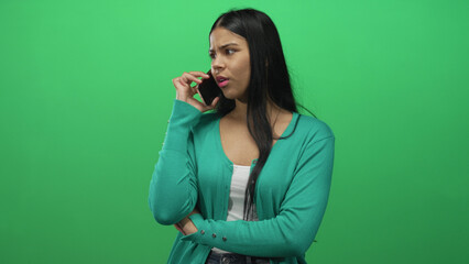 Woman holds smartphone to ear in studio against green screen while crossing arms and looking up;...