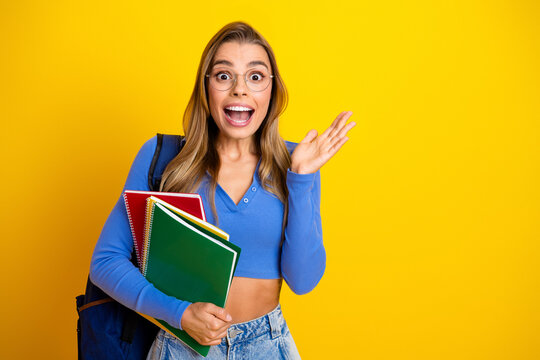 Young female student with backpack holding colorful notebooks smiles against bright yellow background for education lifestyle advertising - Powered by Adobe
