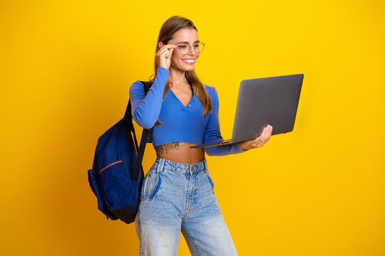 Young woman student with blue top backpack laptop smiling against bright yellow background and casual fashion vibe