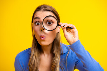 Young woman with magnifying glass exploring fashion and curiosity against a bright yellow background