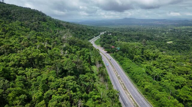 Drone footage of the aerial view of a winding road cutting through lush green forest. Scenic highway number 304 in Thailand links the Bangkok area to Nakhon Ratchasima in the northeastern region