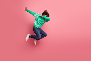 Young man jumps in a green tie dye hoodie against pink background for lifestyle fashion and fitness advertising