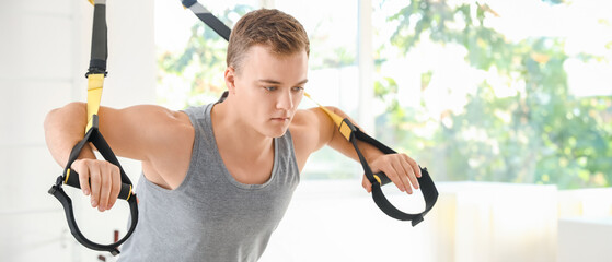 Sporty young man training with TRX straps in gym