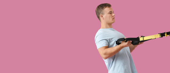Sporty young man training with TRX straps on color background