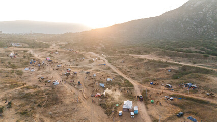 Aerial view of camels and tents at the Pushkar desert cattle fair ground during the Pushkar Fair, with the sun rising through the Aravali mountains in the background, capturing vibrant morning 