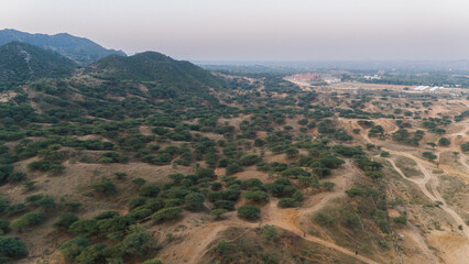 Naklejka premium Aerial view of the Aravali mountains near Pushkar, Rajasthan, showcasing native trees and plants such as Ker, Babool, and Khejri, capturing the lush green hills and natural biodiversity from above.