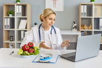 Nutritionist doctor offers telemedicine consultation via laptop. Dietitian explains meal strategies, vegetables highlight healthy choices, advice. Concept: virtual nutrition guidance and care.