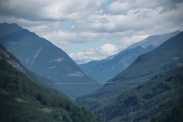 Naklejka premium Majestic mountain valley with dense green forests under a dramatic cloudy sky, showcasing natures grandeur
