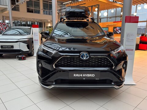 RIGA, LATVIA, DECEMBER 1, 2025: Front view of Toyota RAV4 Hybrid with roof cargo box displayed inside a bright showroom, emphasizing travel and adventure.