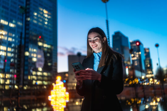 Woman smiling while using phone in city at night - Powered by Adobe