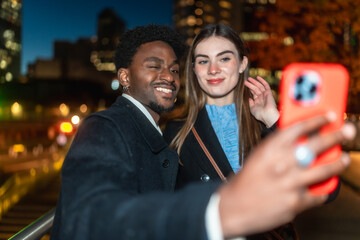 Interracial couple smiling taking selfie in city at night