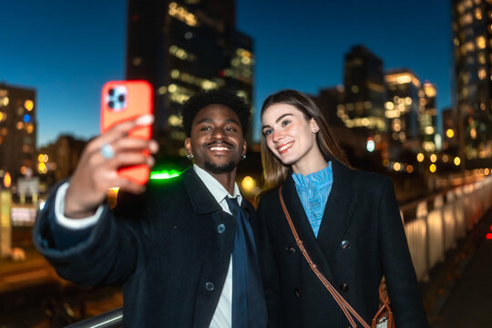 Diverse couple taking selfie enjoying city night lights