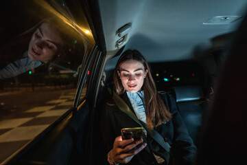 Young businesswoman using smartphone in backseat of car at night