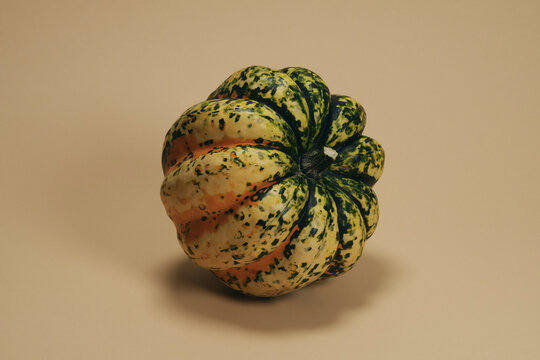 Still life of speckled sweet dumpling squash leaning against beige background
