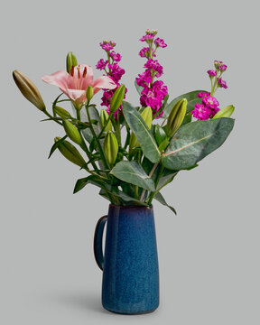 Still life of lily, eucalyptus, and levkoje bouquet in blue pitcher on gray background
