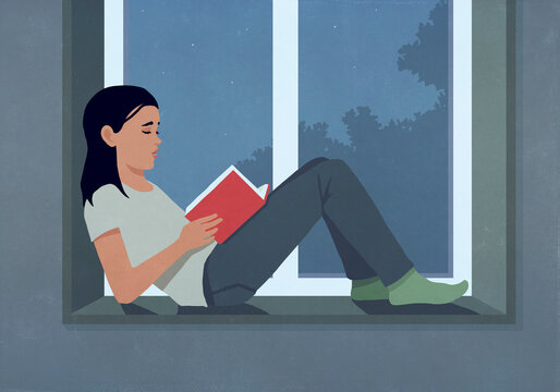 Woman reading book at dark window ledge at night
