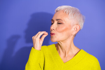 Senior woman with short white hair wearing a bright yellow sweater stands against a purple...