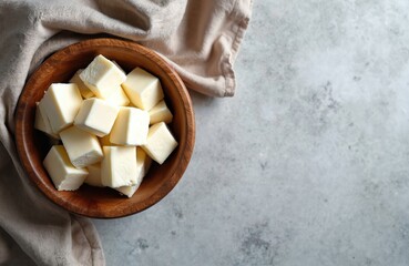Cubes of paneer cheese in wooden bowl. Fresh homemade Indian paneer diced. Culinary photo with dairy product. Healthy vegetarian food ingredient on gray background.