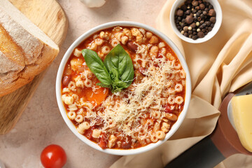 Bowl of pasta fagioli with cheese, basil and peppercorn on beige background