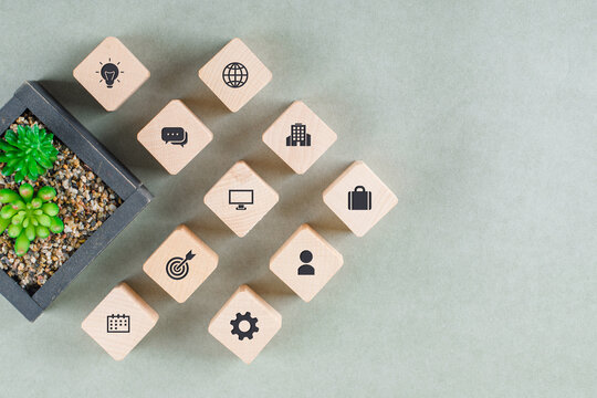 A collection of wooden blocks with various business and technology icons arranged on a textured surface next to a small potted plant and gravel