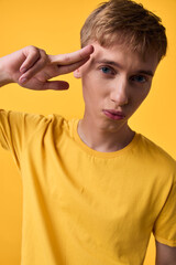 Young man in a yellow t shirt making a peace sign against a matching yellow backdrop, confident casual vibe suitable for lifestyle, fashion, and self expression themes