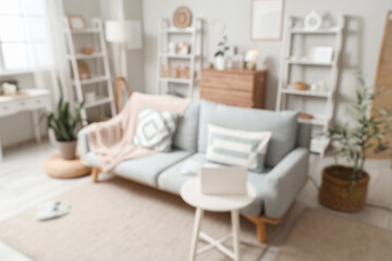 Interior of living room with stylish sofa, shelving units and laptop on coffee table, blurred view