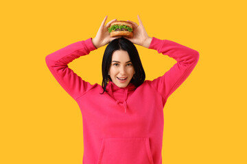 Happy young woman with tasty burger on yellow background