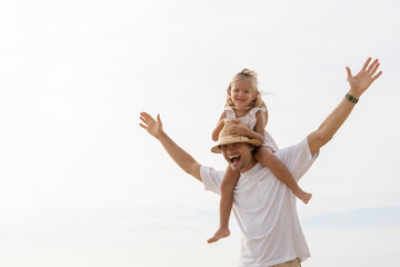 Happy father carrying daughter on shoulders at the beach, both smiling and enjoying summer vacation, representing fatherhood, family bonding, parenting joy and playful lifestyle in tropical setting.