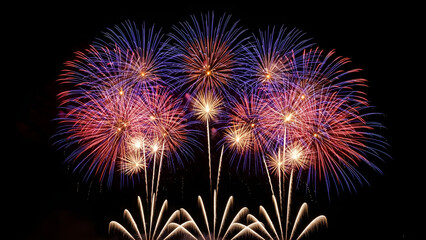Fototapeta premium Colorful fireworks burst across the night sky above the city waterfront, reflecting on the water and creating a grand, vibrant celebration atmosphere.