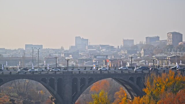 Yerevan Armenia 11.29.2025. A bridge Pobeda over a river with a city in the background. The sky is overcast and the city is full of cars