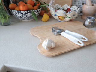 Garlic press on wooden cutting board in kitchen on table. Vintage tableware, traditional objects. Europe, Mediterranean diet, healthy eating.