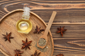 Board with bottle of essential oil, anise stars, dried seeds and spoon on wooden background