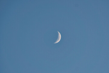 Waxing moon against a clear, blue sky in a calm daylight scene.