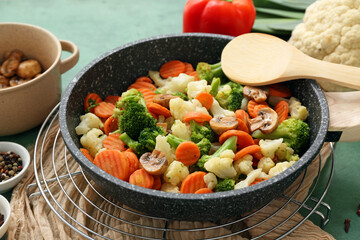 Frying pan with roasted vegetables on green background, closeup