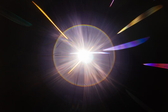 Lens Flare. Light over black background. Easy to add overlay or screen filter over photos. Abstract sun burst with digital lens flare background. Gleams rounded and hexagonal shapes, rainbow halo.