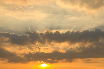 Sunbeams break dramatically through dense clouds in the orange sky.